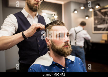 Ritagliato ritratto di barbiere di pettinatura dei capelli del cliente Foto Stock