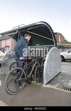 Un ciclista pone la sua bicicletta in una sicura su strada negozio di biciclette ha recentemente installato su una zona residenziale London street. Foto Stock