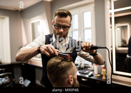 Ritratto di focalizzata barbiere di asciugatura dei capelli del cliente Foto Stock