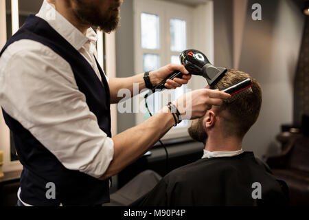 Ritagliato ritratto di barbiere per lo styling dei capelli del cliente con essiccatore Foto Stock