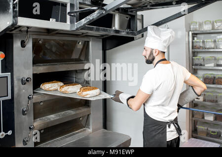 Baker togliere il pane dal forno Foto Stock