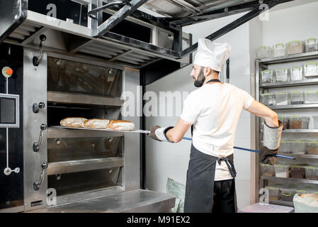 Baker togliere il pane dal forno Foto Stock