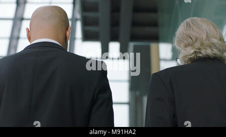 Vista posteriore dei dirigenti aziendali di parlare mentre salite le scale nel moderno edificio per uffici Foto Stock