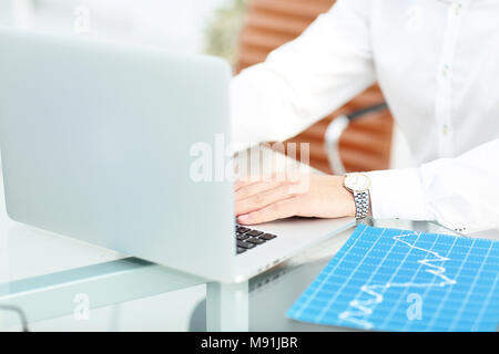 Close up di un imprenditore barbuto con gli occhiali e seduto al computer portatile e la digitazione. Vi è una lavagna e una libreria in background. Foto Stock