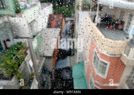 Stagione dei monsoni. close-up di gocce di pioggia sul vetro della finestra. Gocce di acqua di pioggia sulla finestra, scene di strada in background. Ho Chi Minh City. Il Vietnam. Foto Stock