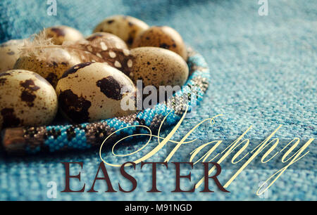 Composizione di pasqua con piuma, uova di quaglia e gioielli di perline su tessuto di lana. Close up. Foto Stock