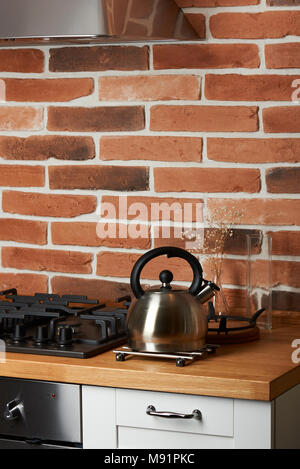 Bollitore in metallo sul moderno tavolo da cucina con rosso Sfondo mattone Foto Stock