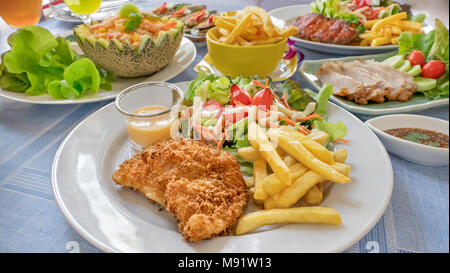 Fritti di pesce serviti bistecca con patate fritte e verdure fresche sulla piastra , e pieno di cibo sul tavolo Foto Stock