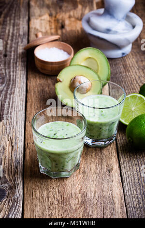 Guacamole stile dip verdura verde smoothie in bicchieri con ingredienti di avocado e calcare sulla tavola in legno rustico, saporito caseificio sano bere con org Foto Stock