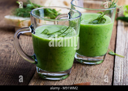 Pisello verde minestra in crema in tazza di vetro con i germogli sulla parte superiore su legno tavolo rustico, sano pasto vegetariano Foto Stock