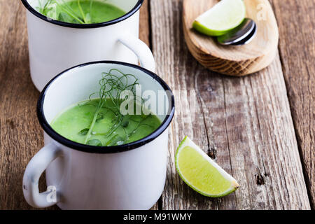 Minestra di crema con pisello verde erbe fresche e i germogli con micro verdi sulla parte superiore nelle zone rurali a tazze, sano pasto vegetariano Foto Stock