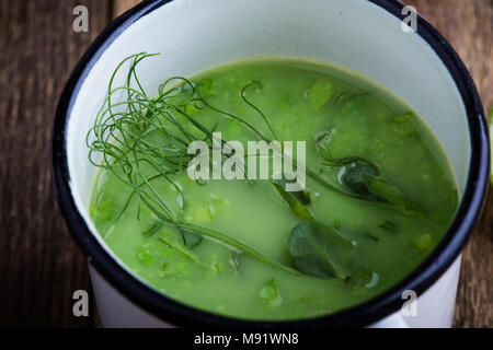 Minestra di crema con pisello verde erbe fresche e i germogli con micro verdi sulla parte superiore nelle zone rurali a tazze, sano pasto vegetariano Foto Stock