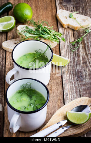 Minestra di crema con pisello verde erbe fresche e i germogli con micro verdi sulla parte superiore nelle zone rurali a tazze, sano pasto vegetariano Foto Stock