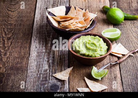 Guacamole fresco dip con il succo di lime servito con nachos fatti a mano in legno tavolo rustico e tradizionale stile messicano salsa di avocado nel recipiente di ceramica, healt Foto Stock