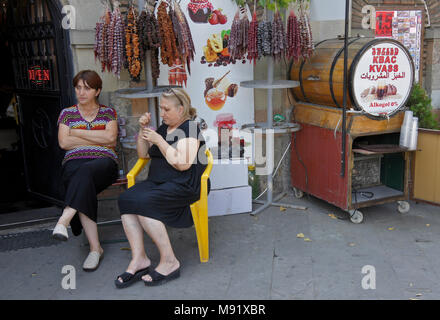 Due donne siedono al di fuori di un negozio che vende Churchkhela (Churchxela), fresche, miele e bevande locali da una canna, Tbilisi, Georgia Foto Stock