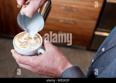 Professional barista versando latte vaporizzato da acciaio inossidabile lo sbarramento rotante nella tazza da caffè rendendo latte art sul cappuccino Foto Stock