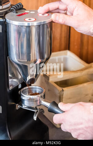 Barista portafilter tenuta in mano e la macinazione di chicchi di caffè con la fresa per fare caffè espresso o cappuccino Foto Stock