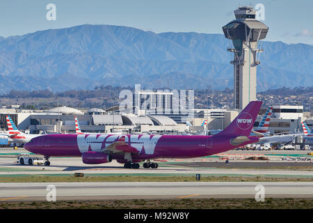 WOW Air Airbus A330-300 trainato per il Tom Bradley Terminal presso l'Aeroporto Internazionale di Los Angeles LAX, la torre di controllo e le montagne alle spalle. Foto Stock