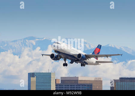 Delta Air Lines Airbus A319 aereo di linea che decollano dall'Aeroporto Internazionale di Los Angeles LAX, nuvole e la coperta di neve Montagne di San Gabriel dietro. Foto Stock