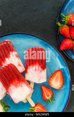 In casa Vegan Fragola ghiaccioli con succo di fragola e latte di cocco in marmo scuro dello sfondo. In estate il concetto di cibo. Vista dall'alto. Foto Stock