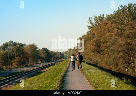 Varsavia, Polonia : vista posteriore di un uomo e di una donna in bicicletta lungo la via lastricata, attraverso la campagna polacca. Tranquilla scena d'autunno al crepuscolo Foto Stock