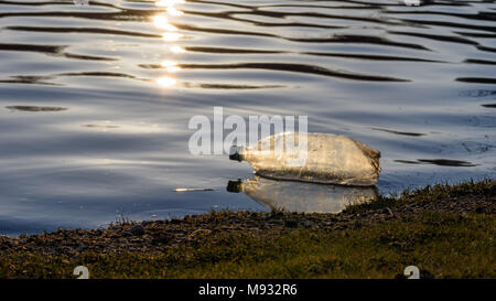 Singola bottiglia d'acqua in plastica per lettiera floating lungo il litorale al tramonto Foto Stock