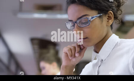 Razza mista femmina in occhiali pensando a progetto presso ufficio, nuove idee Foto Stock