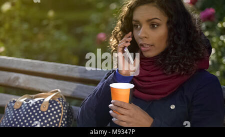 Attraente razza mista Donna che parla al telefono e di bere il caffè all'aperto Foto Stock