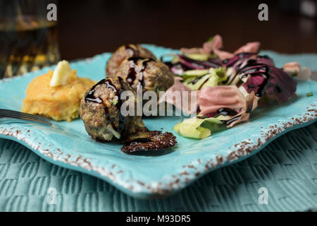 Di colore rosa e verde insalata di radicchio, purè di patate e patate dolci con burro e una spruzzata di aceto balsamico polpette di carne cotta al forno servita su un quadrato piatto rustico Foto Stock