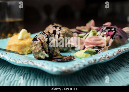 Di colore rosa e verde insalata di radicchio, purè di patate e patate dolci con burro e una spruzzata di aceto balsamico polpette di carne cotta al forno servita su un quadrato piatto rustico Foto Stock