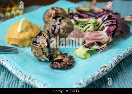 Di colore rosa e verde insalata di radicchio, purè di patate e patate dolci con burro e una spruzzata di aceto balsamico polpette di carne cotta al forno servita su un quadrato piatto rustico Foto Stock