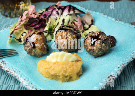 Di colore rosa e verde insalata di radicchio, purè di patate e patate dolci con burro e una spruzzata di aceto balsamico polpette di carne cotta al forno servita su un quadrato piatto rustico Foto Stock