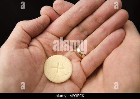 Mani a tazza di un uomo con una fetta di pane il Corpo di Cristo quando si riceve la comunione a Roman Catholic Mass Foto Stock