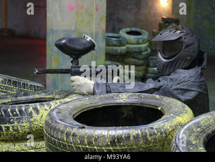 Un uomo con un marcatore per il paintball nei boschi seduta per pneumatici in agguato. Foto Stock