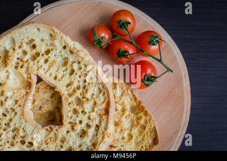 Italiano di pane secco Friselle sulla tavola di legno con pomodori ciliegia. Il cibo italiano. Una sana alimentazione vegetariana. Foto Stock