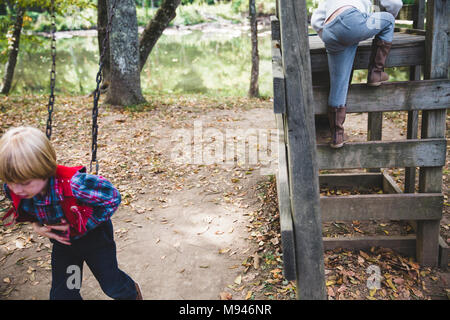 Ragazzo giocando con swing con la ragazza salendo accanto a lui Foto Stock