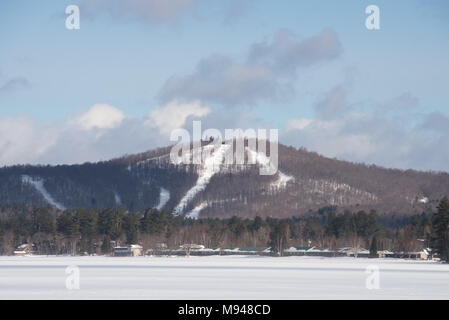 Una vista di Oak Mountain Ski Hill dal lago piacevole nelle Montagne Adirondack, NY con neve, ghiaccio, un cielo blu di sfondo e copiare lo spazio. Foto Stock