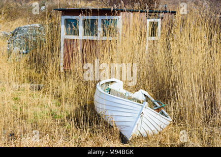 Vecchio e stagionato canotto bianco sul terreno di fronte ad un piccolo capannone quasi nascosta in reedbed. Foto Stock