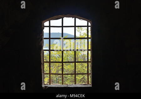 Finestra con le sbarre di una prigione abbandonata con una vista al verde degli alberi e il mare Foto Stock