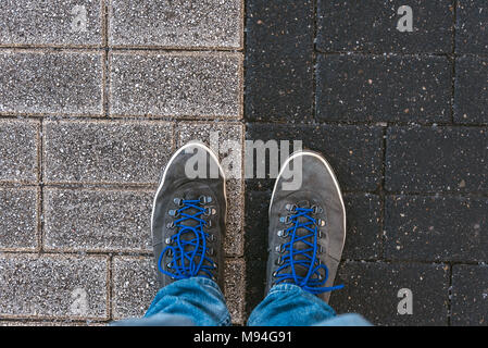 Fino a raggiungere un incrocio a dover decidere circa il passato, ora e in futuro simboleggiato da due piedi e scarpe in piedi su due diversi colori sul percorso da ab Foto Stock