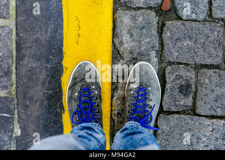 Fino a raggiungere un incrocio a dover decidere circa il passato, ora e in futuro simboleggiato da due piedi e scarpe in piedi su due differenti materiali percorso da abo Foto Stock