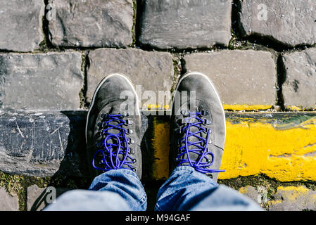 Fino a raggiungere un incrocio a dover decidere circa il passato, ora e in futuro simboleggiato da due piedi e scarpe in piedi su due differenti materiali percorso da abo Foto Stock