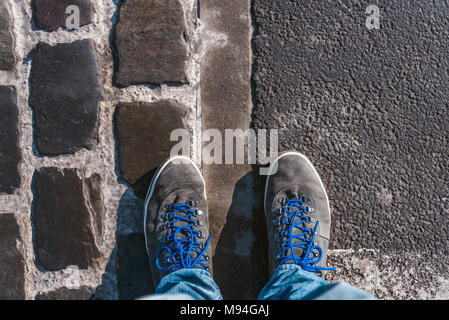 Fino a raggiungere un incrocio a dover decidere circa il passato, ora e in futuro simboleggiato da due piedi e scarpe in piedi su due differenti materiali percorso da abo Foto Stock