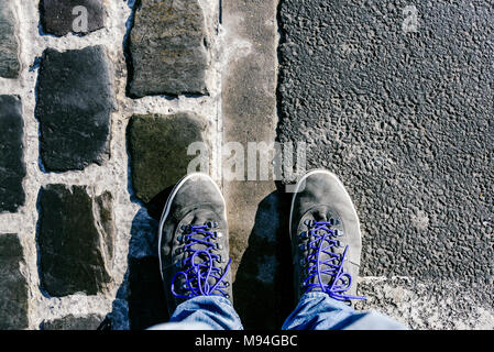 Fino a raggiungere un incrocio a dover decidere circa il passato, ora e in futuro simboleggiato da due piedi e scarpe in piedi su due differenti materiali percorso da abo Foto Stock