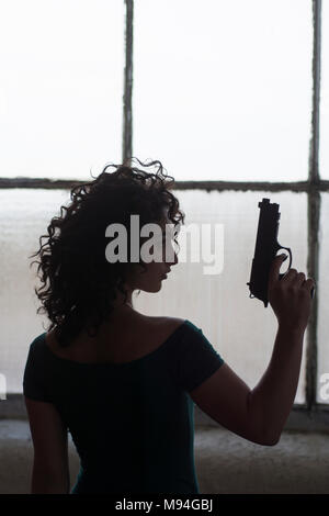 Giovane donna in possesso di una pistola mediante la finestra Foto Stock