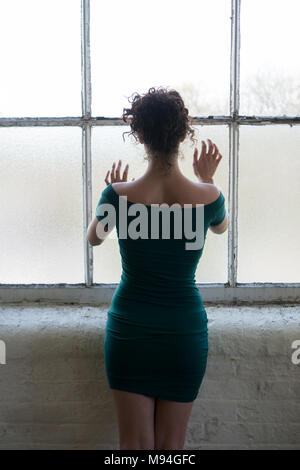 Vista posteriore di un solitario donna in piedi dalla finestra mani toccano il vetro Foto Stock