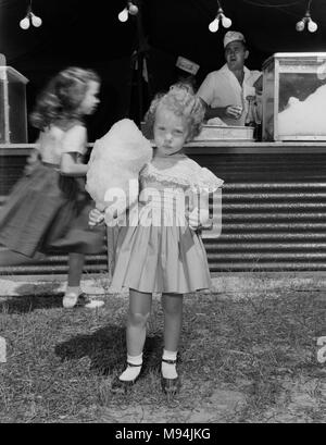 Un grave bambina mantiene la sua caramella di cotone mentre in un circo in Georgia rurale, ca. 1960. Foto Stock