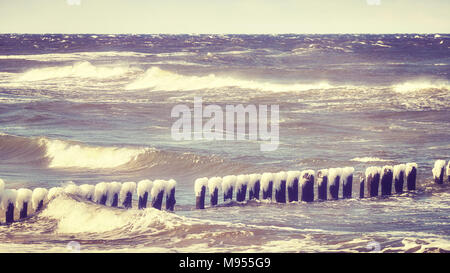 Congelati frangiflutti in legno in una giornata di vento, del Mar Baltico della Polonia, dai toni di colore dell'immagine. Foto Stock