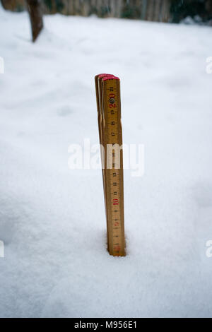 Un vecchio righello di legno pieghevole fuori della neve in un giardino misura la profondità di nevicata a circa quattro centimetri Foto Stock