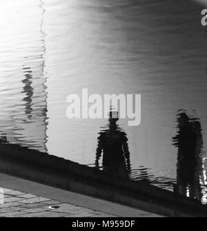 Riflessioni di due persone sulla superficie ondulata di un canale nella città di Milano, Italia Foto Stock